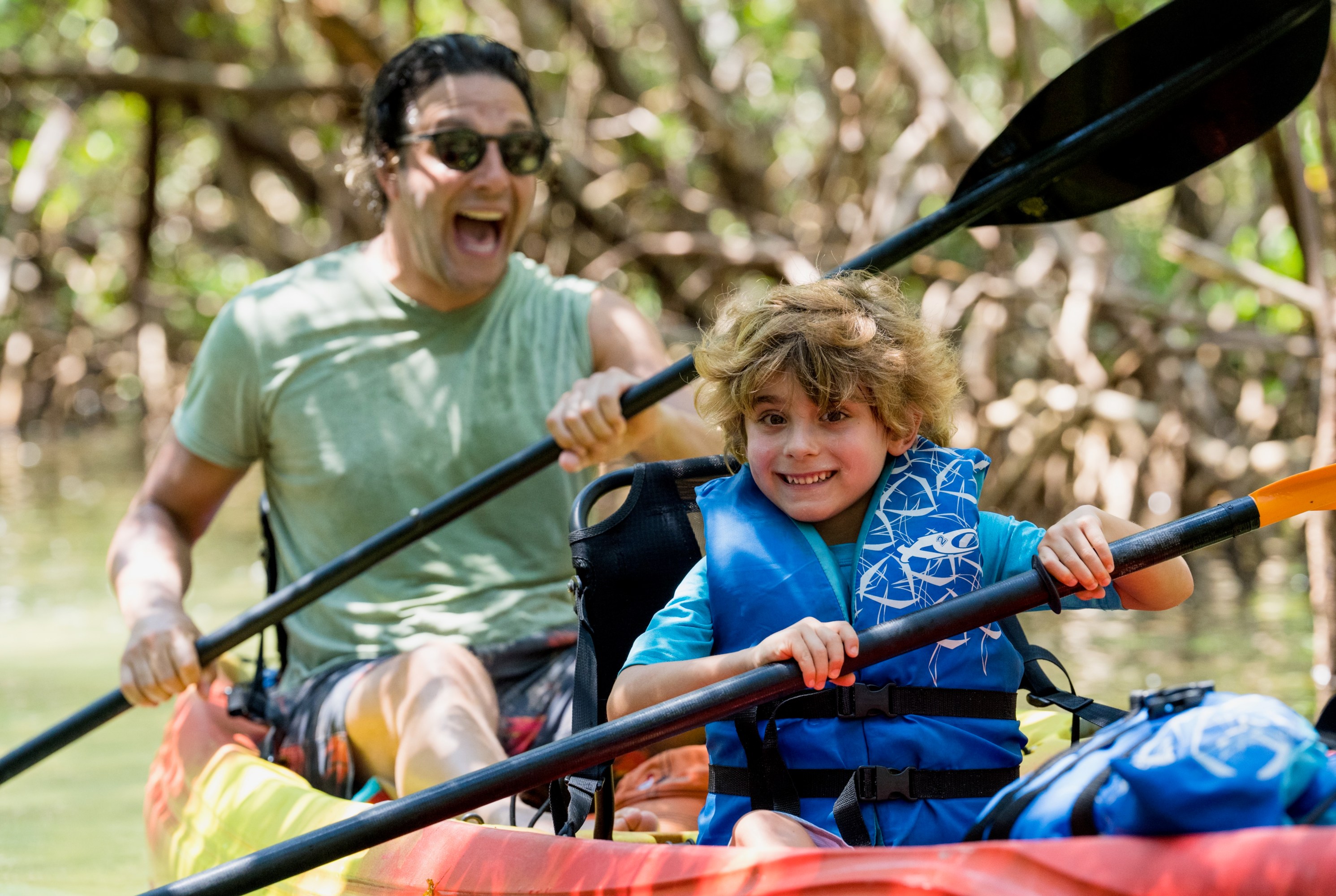 Man and child kayaking in mangrove, smiling.