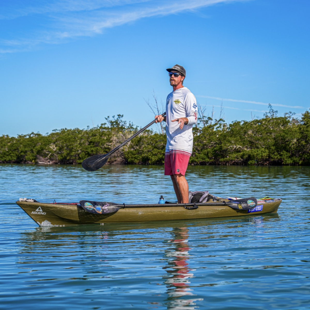 Person kayaking on calm water under blue sky near trees.