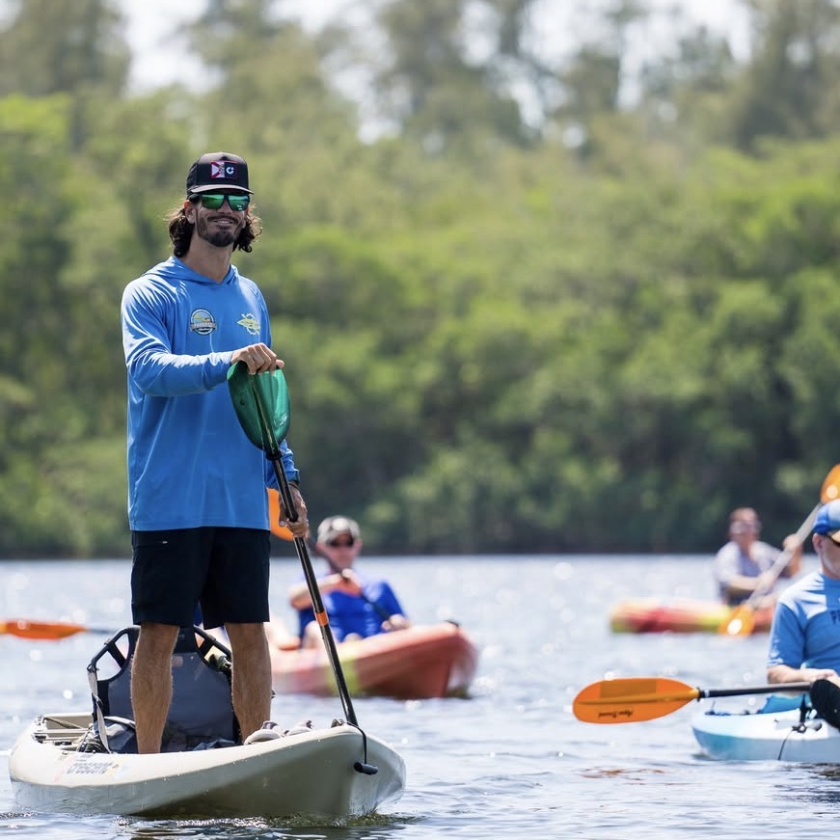 Group kayaking on a calm lake with lush green trees in the background.
