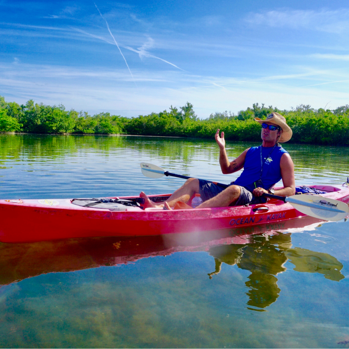 Person paddling a red kayak on calm water under a clear blue sky.